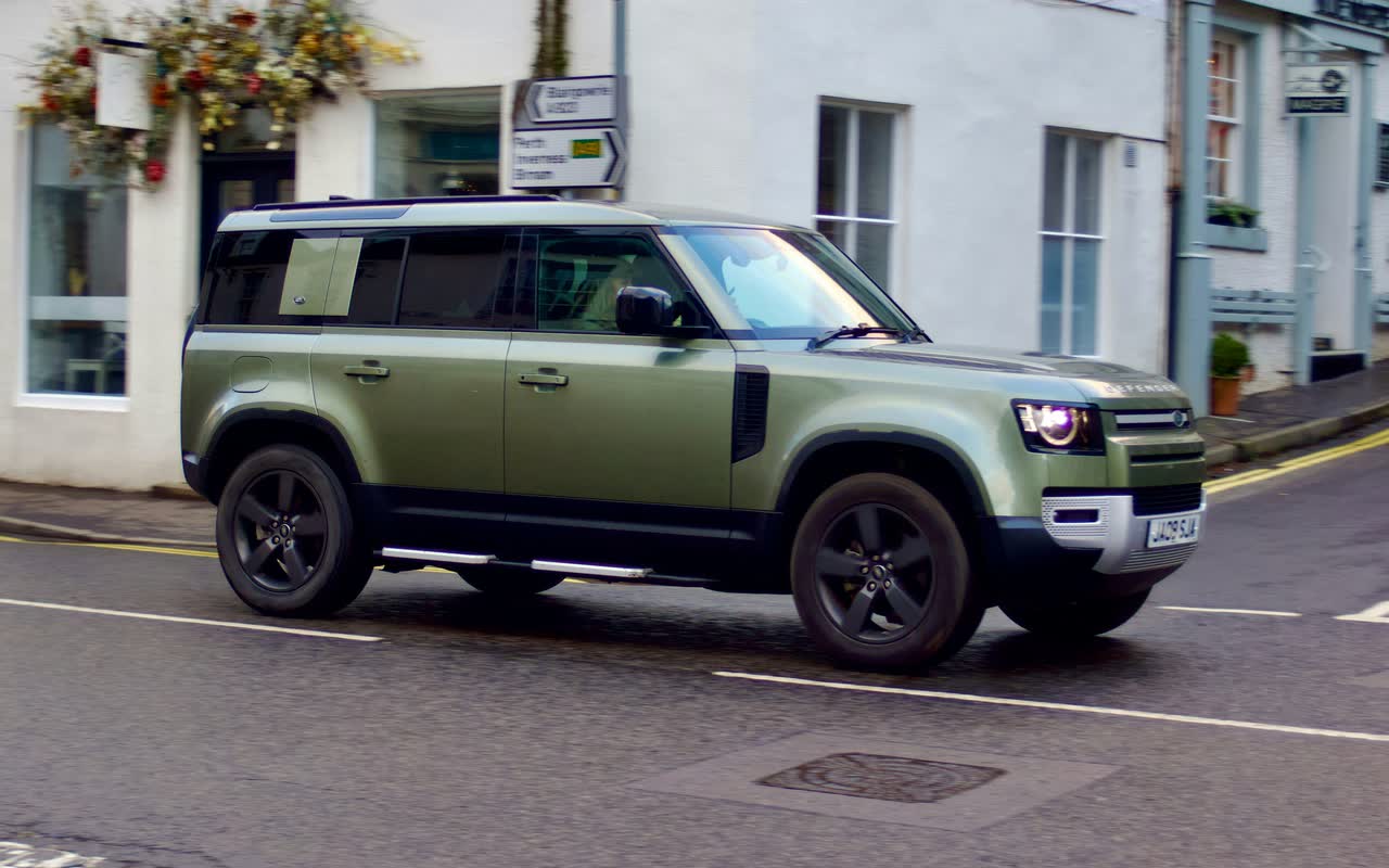 Зелёный Land Rover Defender 110 на улице с белыми домами
